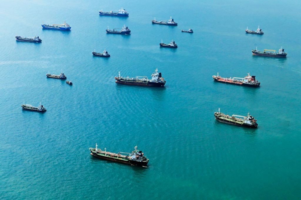heros-img Numerous cargo ships anchored on the blue ocean, captured from above.