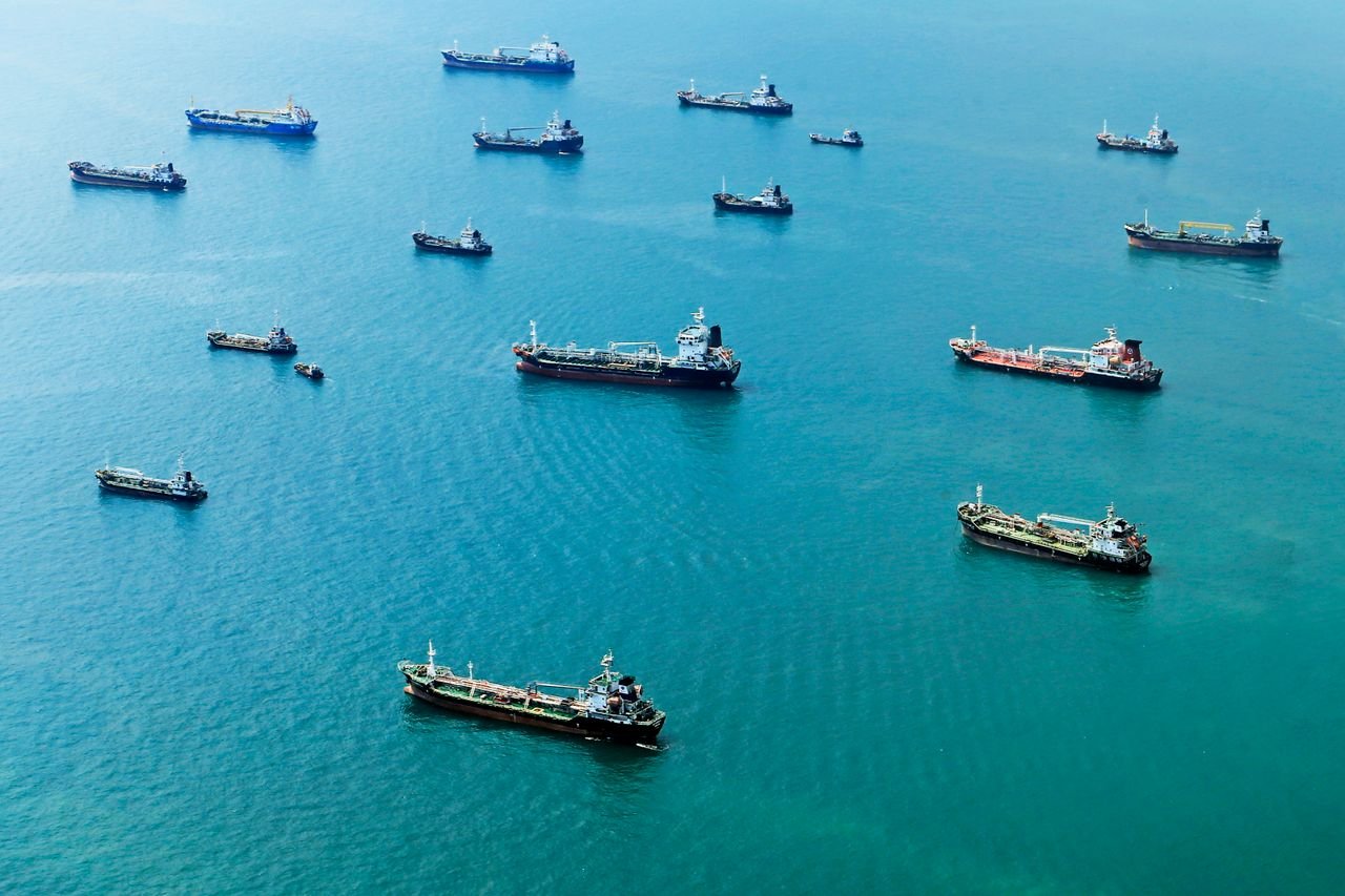 Numerous cargo ships anchored on the blue ocean, captured from above.